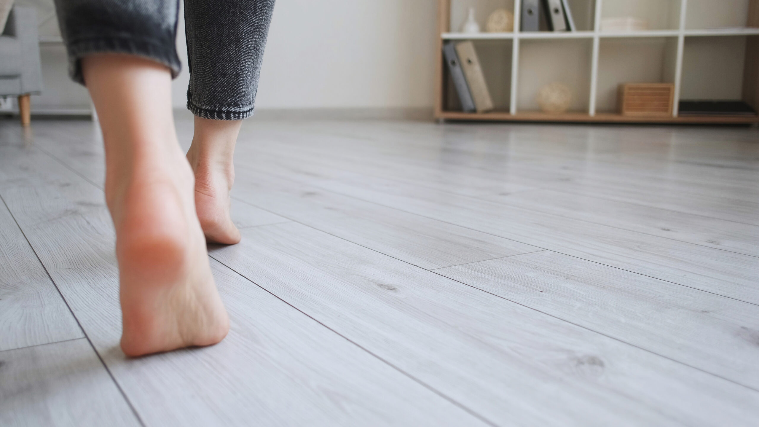 Floor heating. Home barefoot. Unrecognizable woman feet walking on warm laminate flooring wood panels modern flat interior with copy space