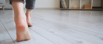 Floor heating. Home barefoot. Unrecognizable woman feet walking on warm laminate flooring wood panels modern flat interior with copy space